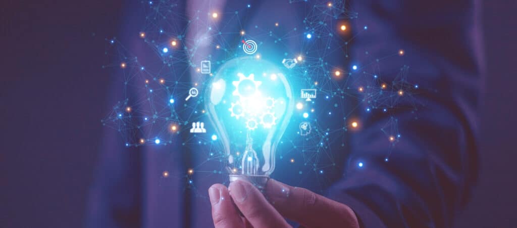 A hand holding a glowing lightbulb with interconnected business icons and a gear symbol inside, representing innovative solutions for recruitment agencies and back office outsourcing.