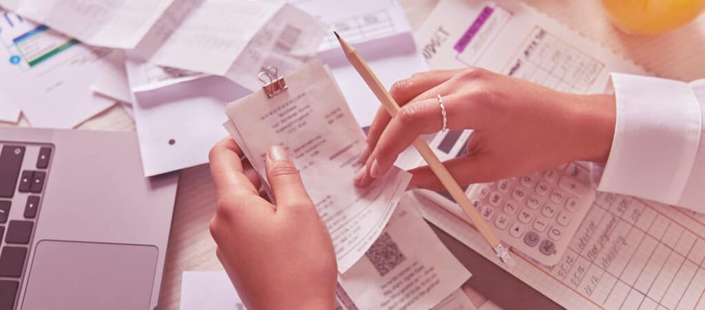 A person sorting through a cluttered pile of receipts and invoices for bookkeeping, highlighting common accountancy services challenges faced by recruitment agencies when identifying non-claimable business expenses.