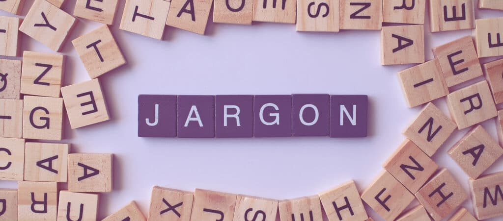 Purple letter tiles spelling the word 'JARGON' surrounded by scattered wooden blocks, representing the need for recruitment agencies to simplify complex financial terms through professional accountancy services.