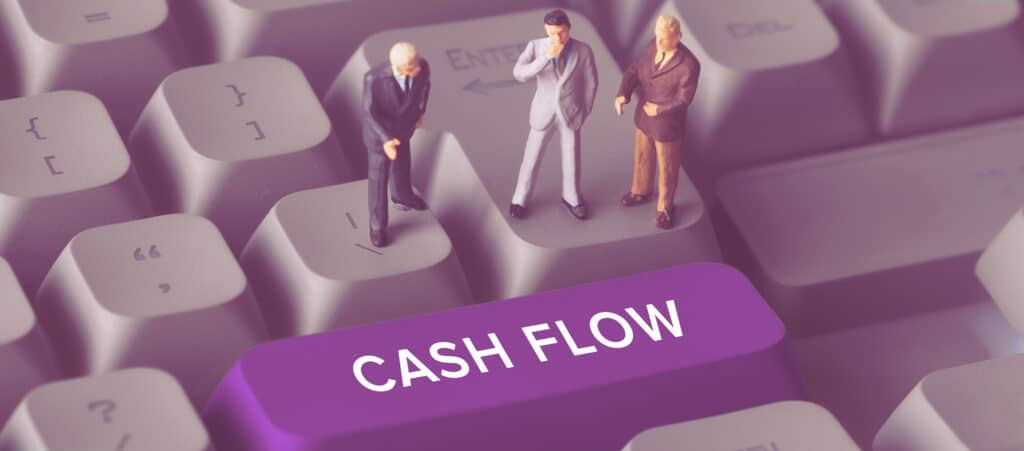 Miniature business figures standing on a keyboard next to a purple CASH FLOW button, illustrating recruitment agency working capital challenges.